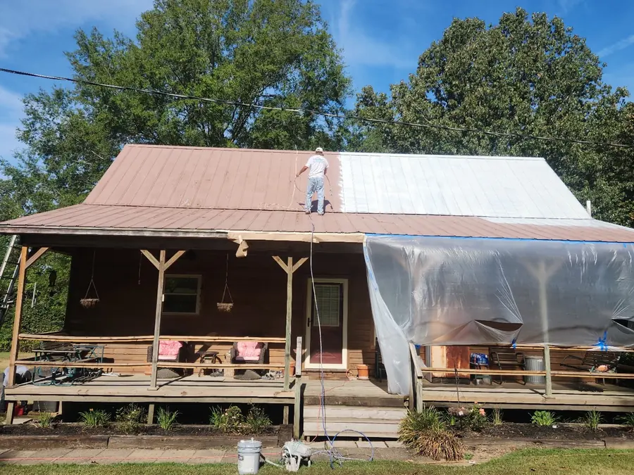 Dario spraying the metal roof of a house with a covered front porch
