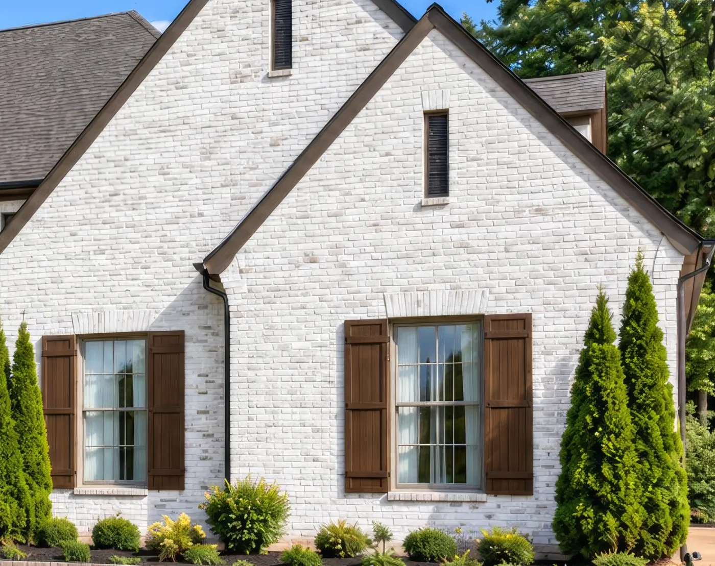 A house of painted white brick with dark wood shutters and tall windows