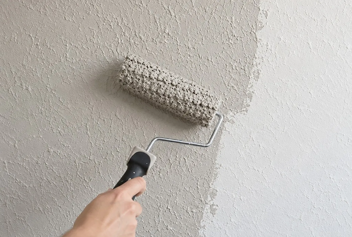 A roller on a textured knockdown wall, side light showing the texture