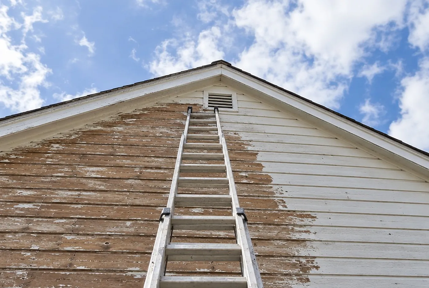 A tall two-story gable end with an extension ladder reaching toward the peak