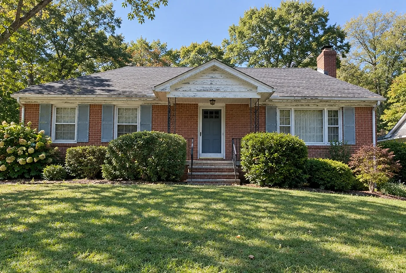 A brick ranch house with peeling white trim and sun-faded shutters
