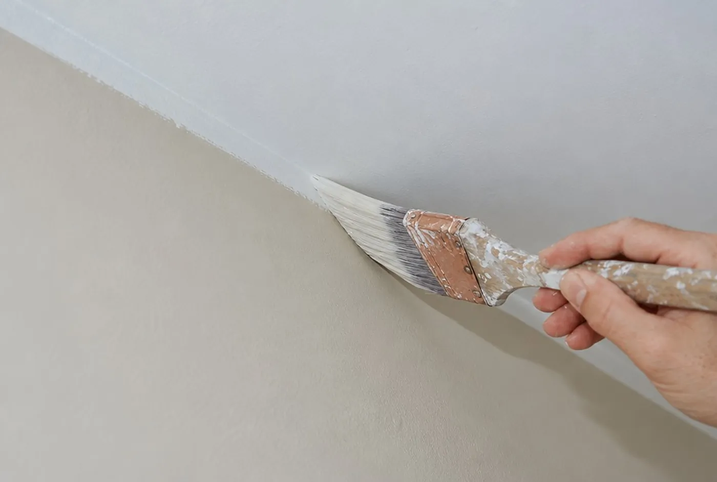 An angled brush cutting a straight line where a greige wall meets a white ceiling