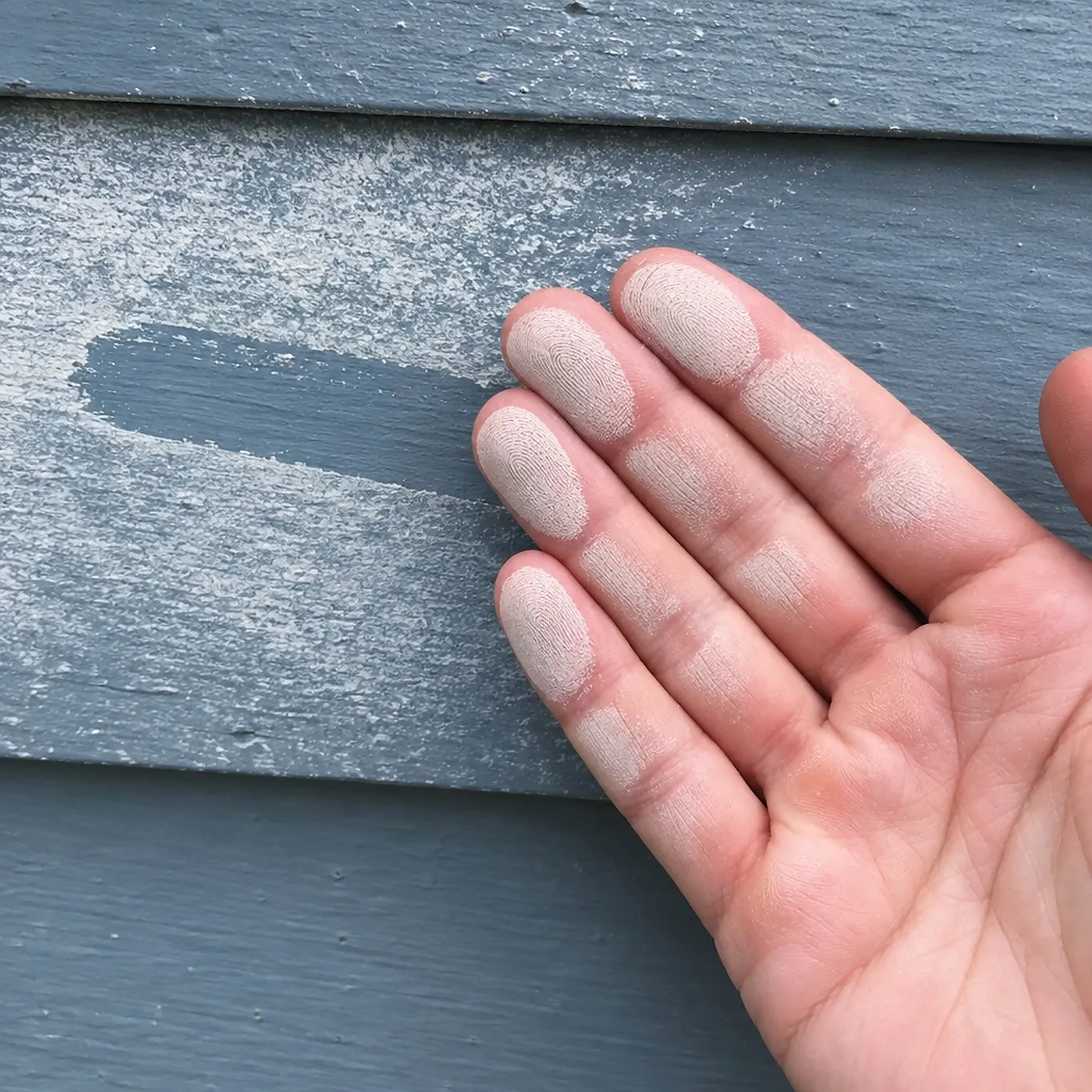 A fingertip wiped through white chalk on painted siding