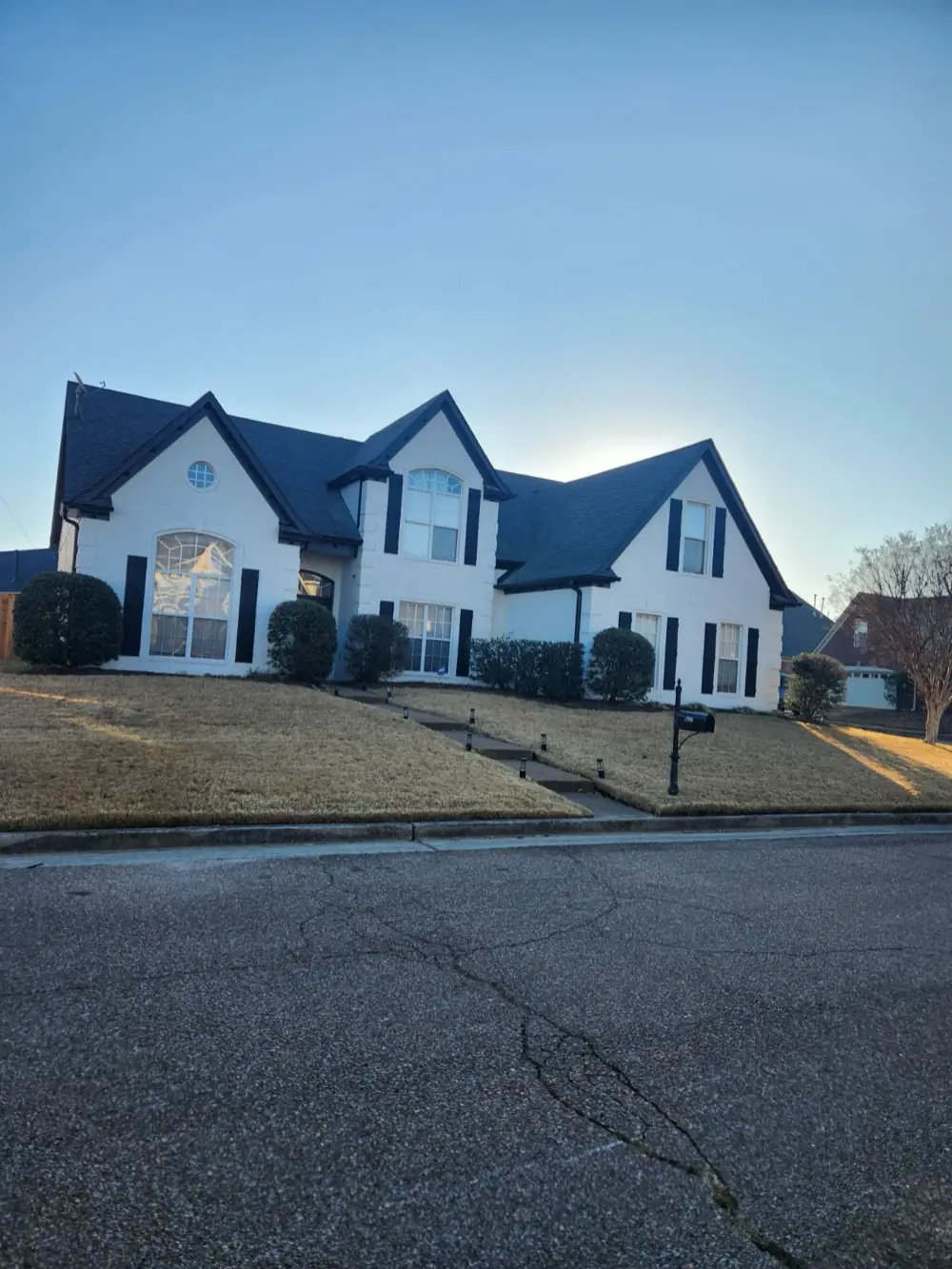A two-story Memphis home with its brick painted white, black shutters and dark trim